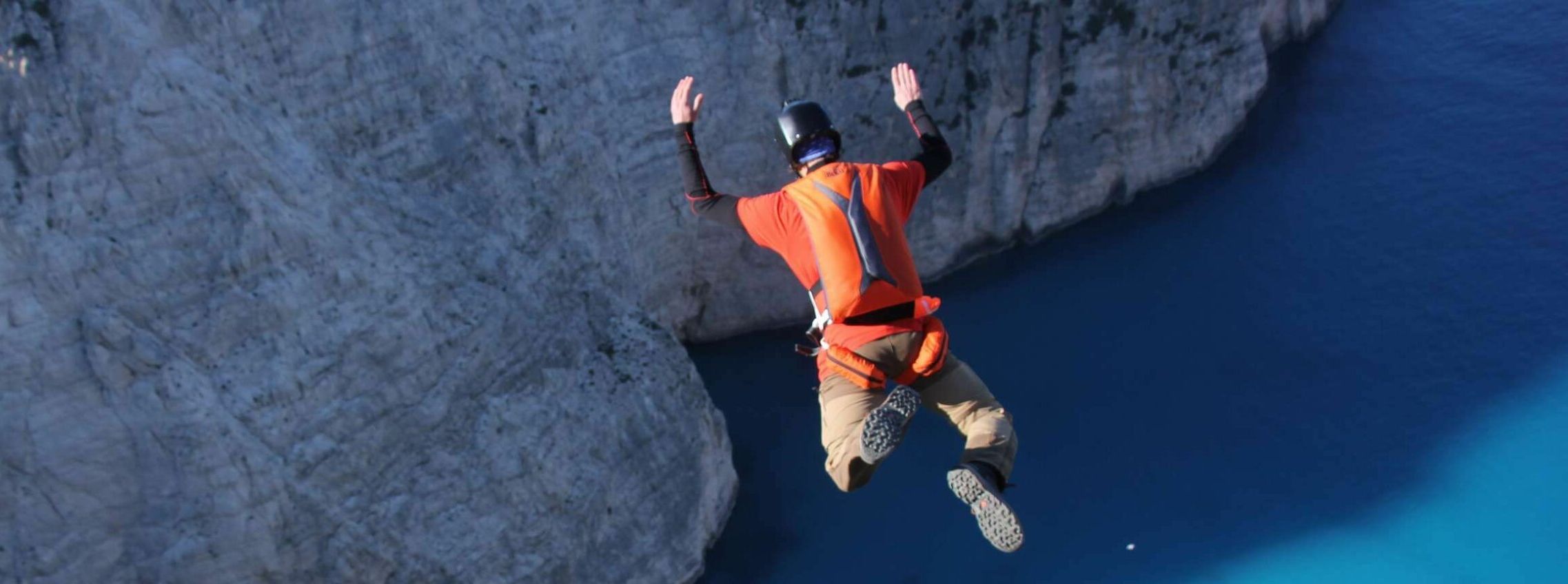 Un base jumper s'élançant dans le vide vu depuis le dessus, il porte un parachute orange adrenalin base.